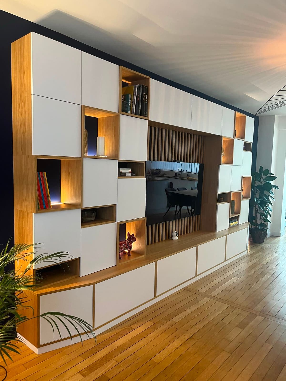 Bibliothèque murale à niches éclairées, TV intégrée et claustra bois, sur parquet à chevrons