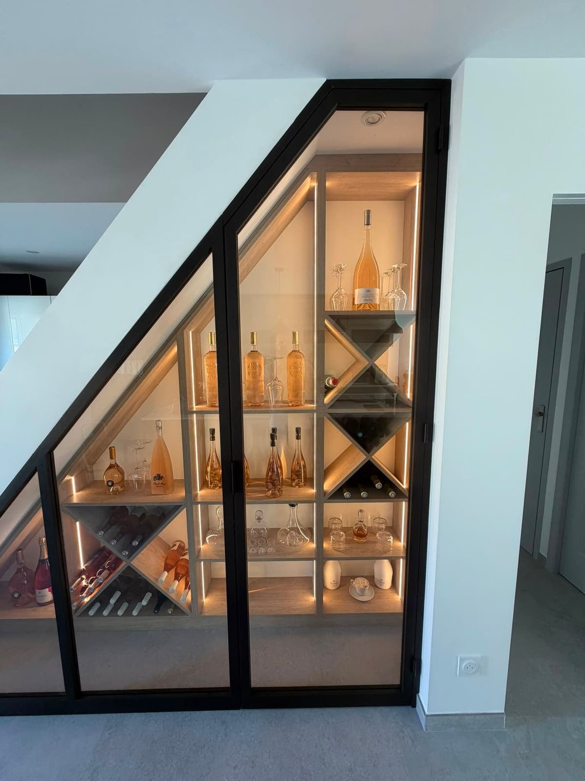 Intérieur de la cave à vin sous escalier : casiers en croisillons et étagères à bouteilles