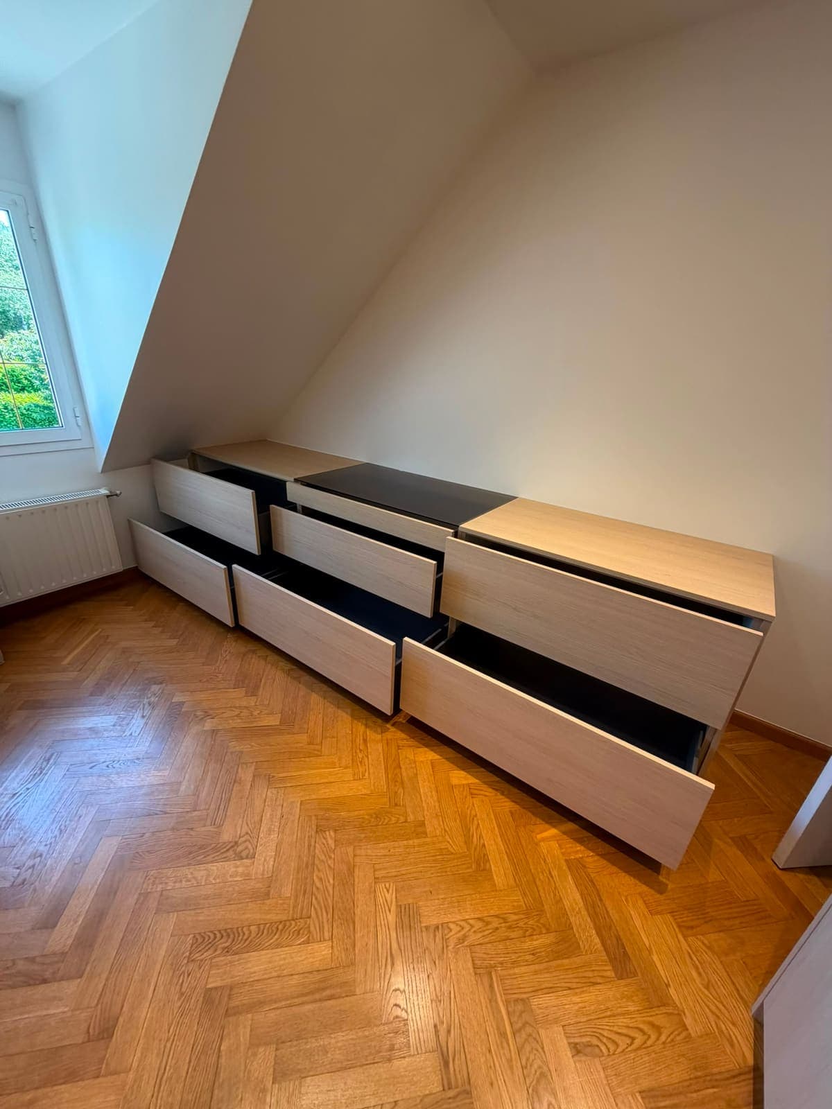 Commode sur mesure aux tiroirs ouverts, calée sous un rampant de toiture