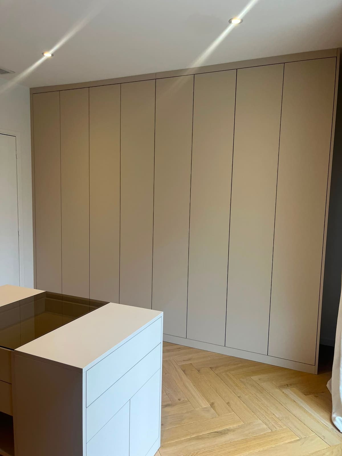 Dressing mur à mur du sol au plafond, façades rainurées beige sur parquet à chevrons