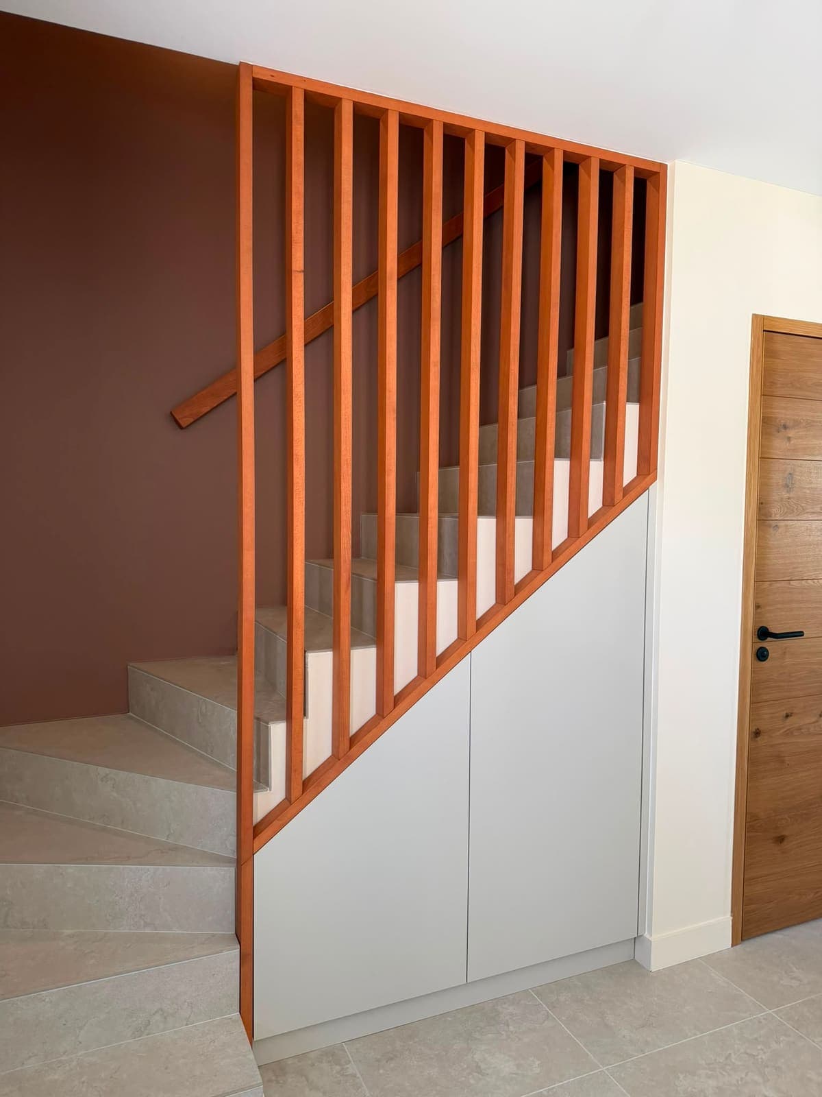 Garde-corps claustra bois et placards blancs sous escalier, contre un mur terracotta
