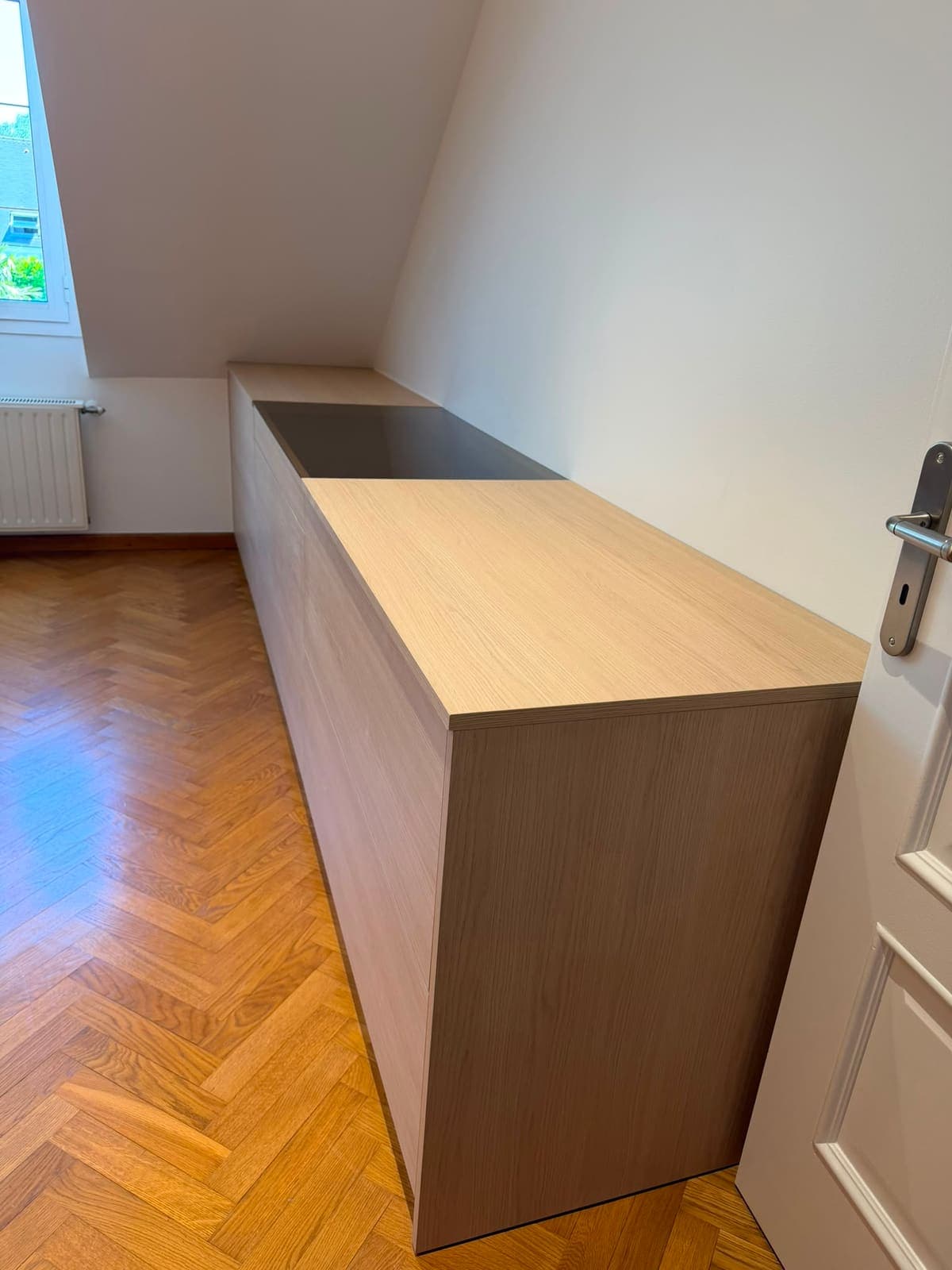 Meuble bas à plan de travail bois installé sous la pente d'une chambre mansardée