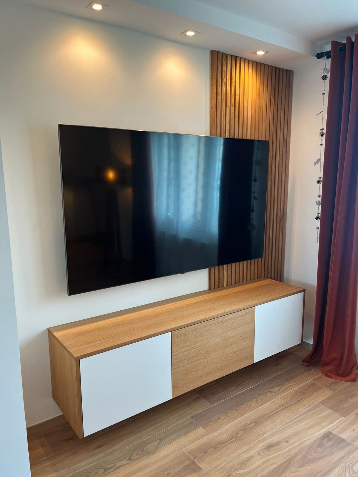 Meuble TV bas bois et blanc devant un mur habillé de tasseaux verticaux