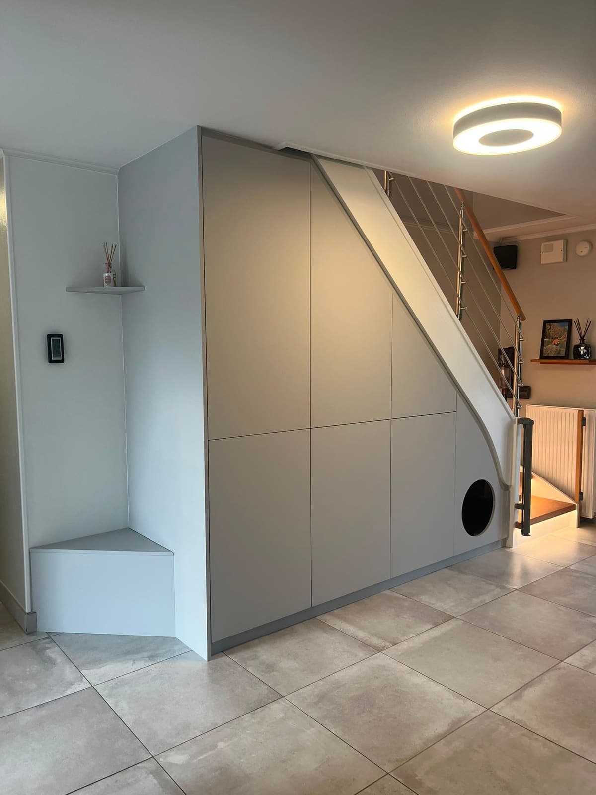 Placards blancs sans poignée sous un escalier, prolongés par un banc d'assise