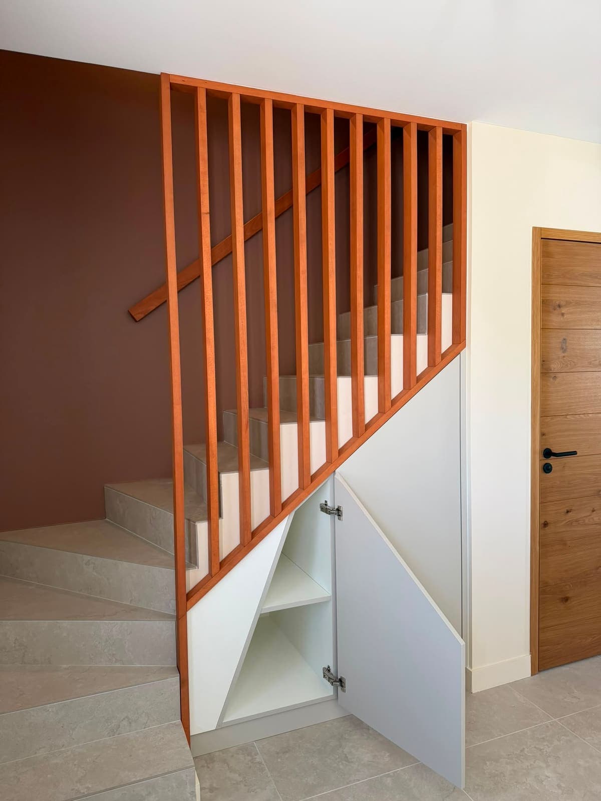 Porte triangulaire ouverte sur le rangement aménagé dans l'angle bas d'un escalier