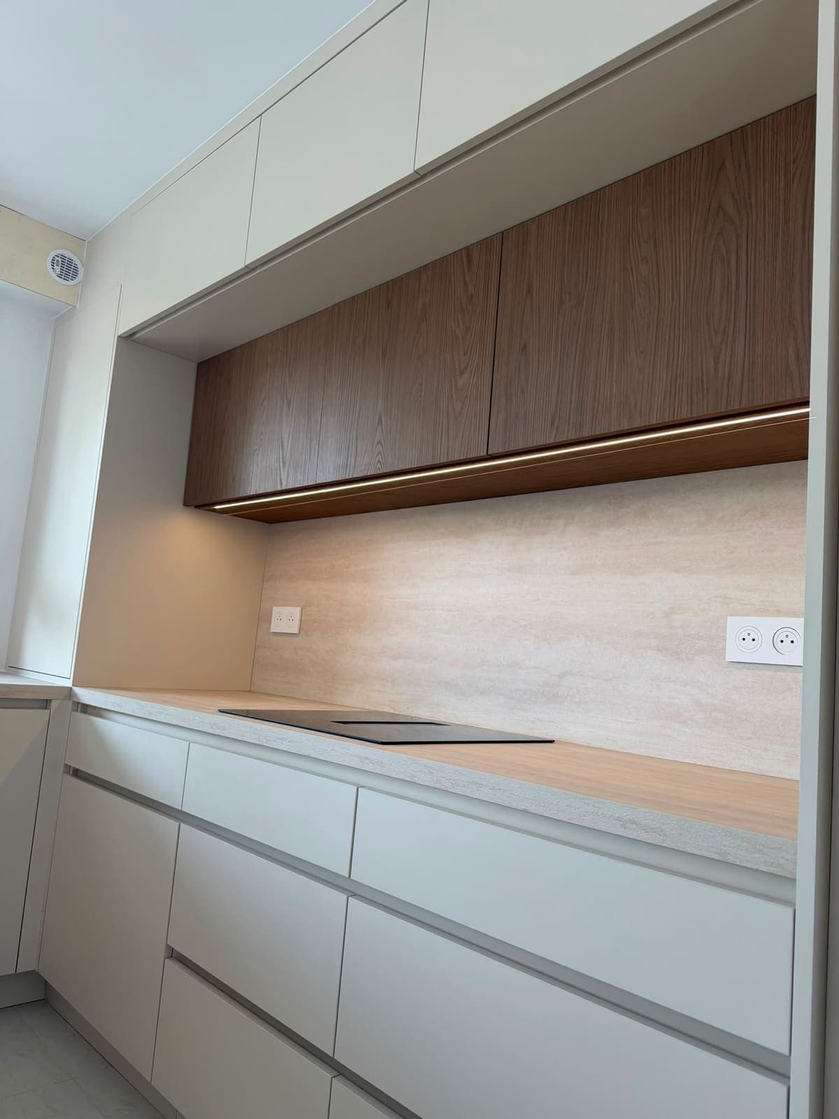 Cuisine blanche sous pente avec meubles hauts en noyer et bandeau LED sous les caissons